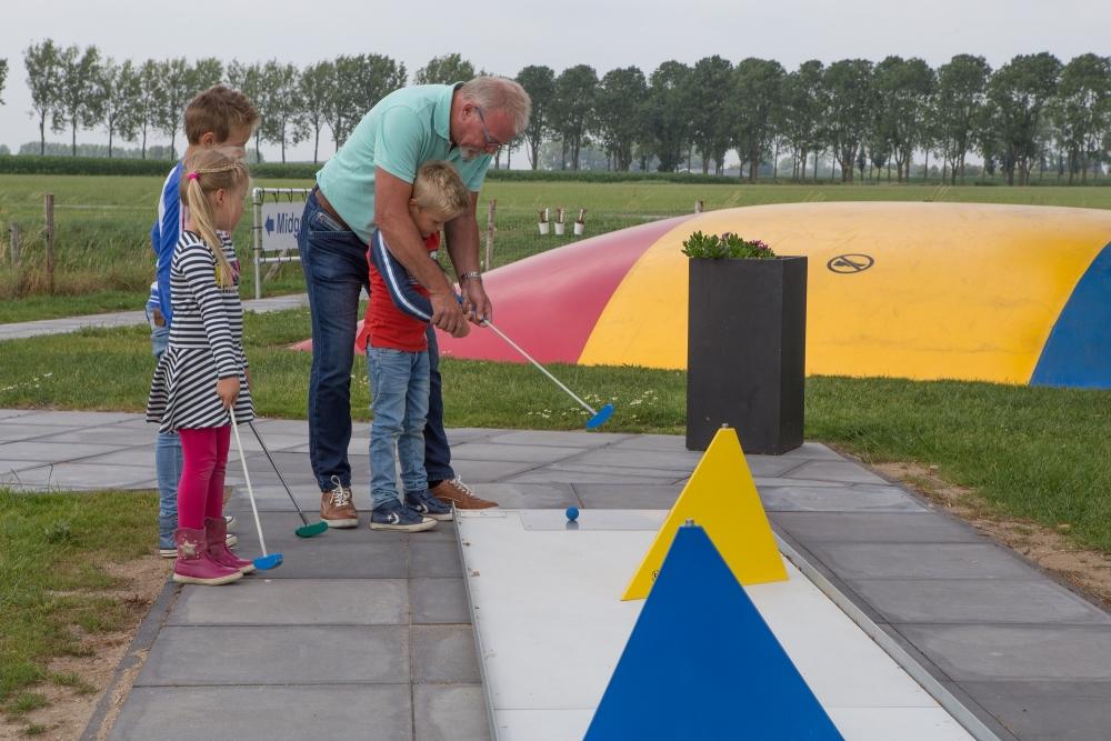 Opa leert de kinderen hoe ze midgetgolf moeten spelen